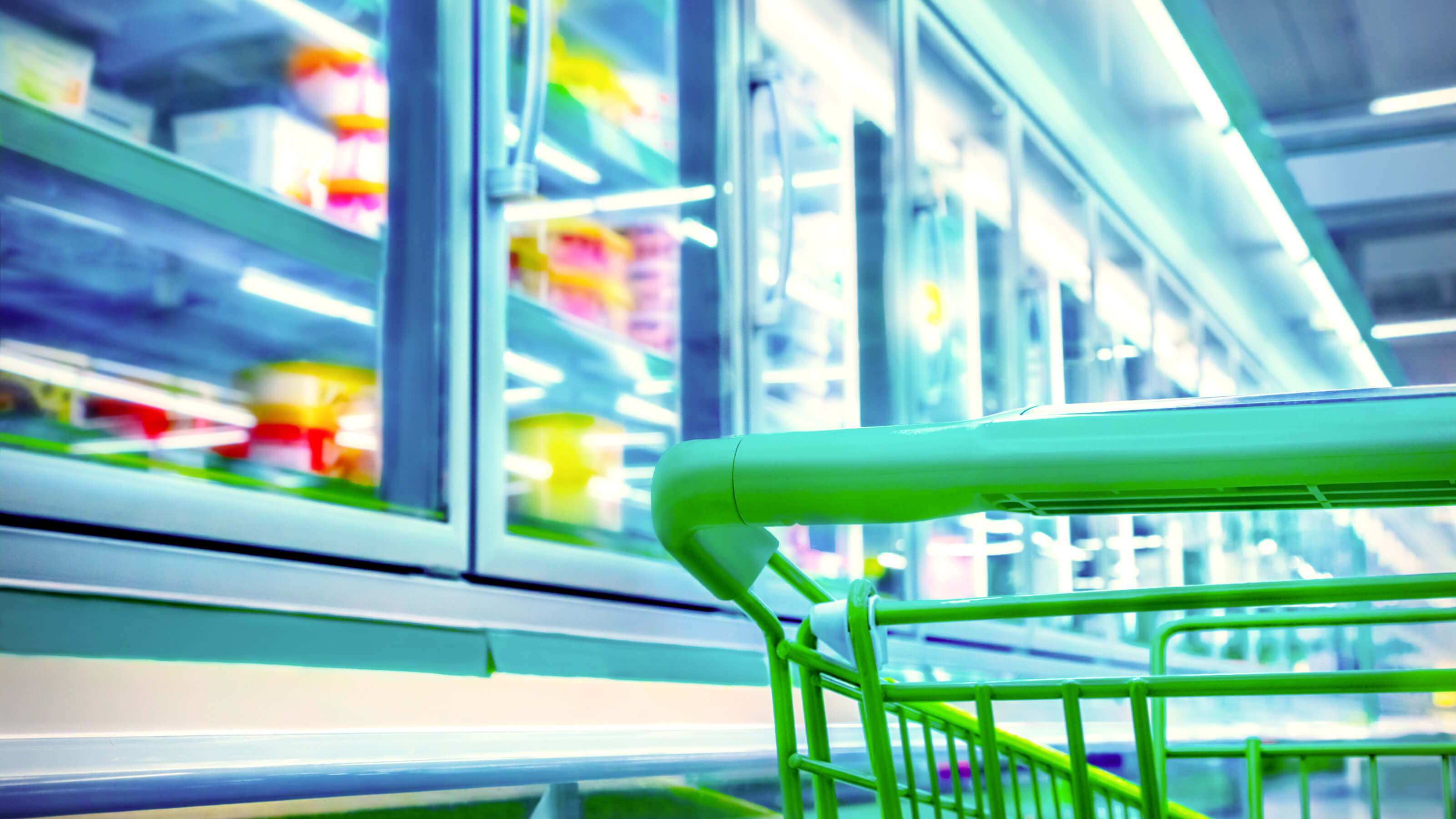 A shopping cart located in front of a refrigerator displaying frozen food products in a grocery store aisle.