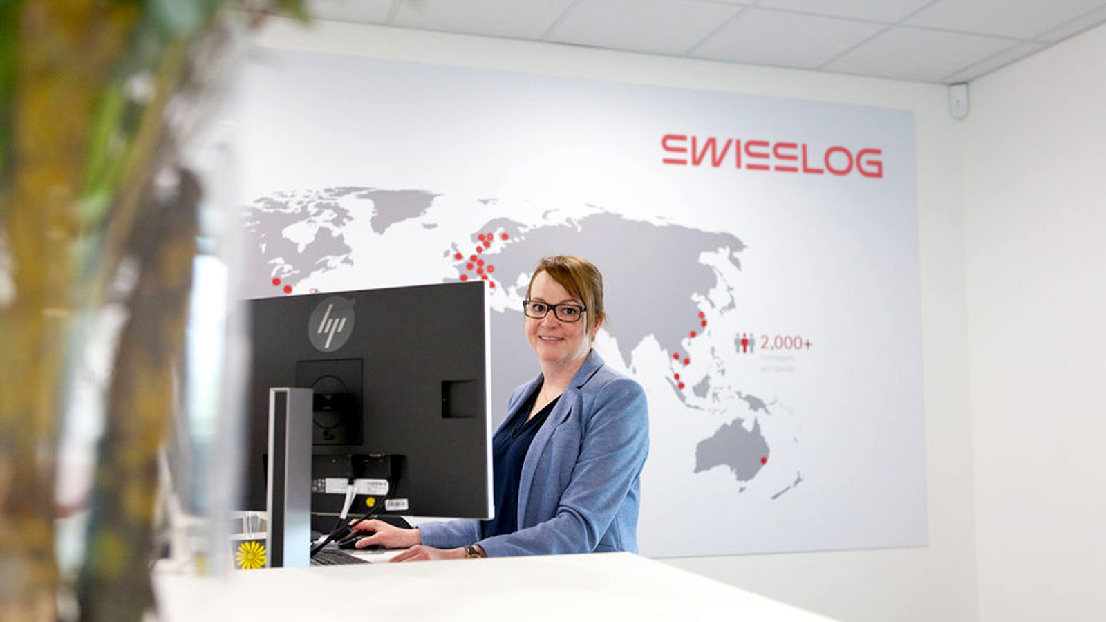 Swisslog employee in a reception with office locations shown behind